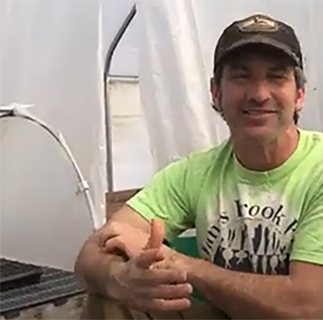 Picture of farmer in a green shirt and ball cap talking to the camera in a high tunnel