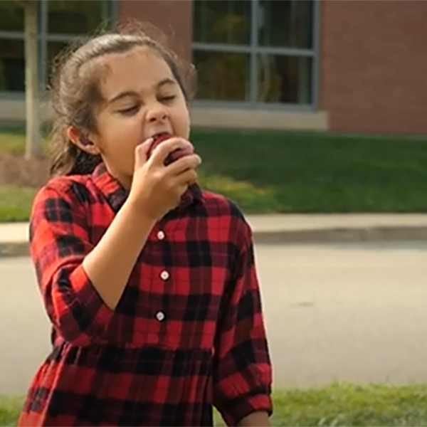 girl in front of a building crunching into an apple