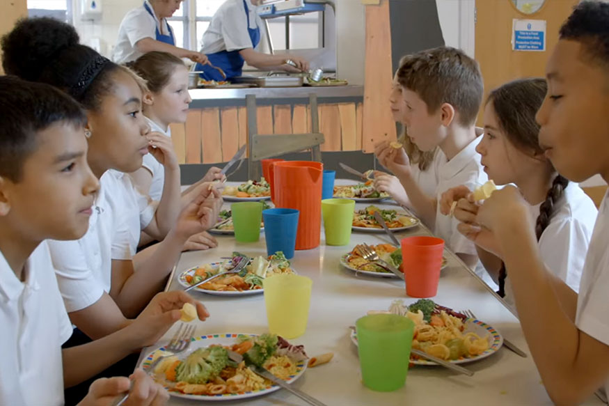 kids sitting at a cafeteria table eatingl unch
