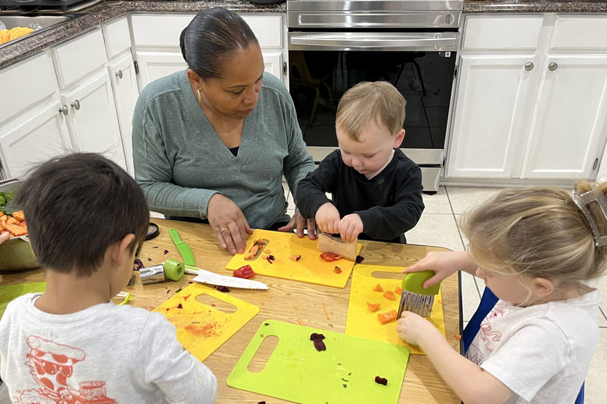 Woman teaching toddlers how to prepare sweet potatoes in a kitchen