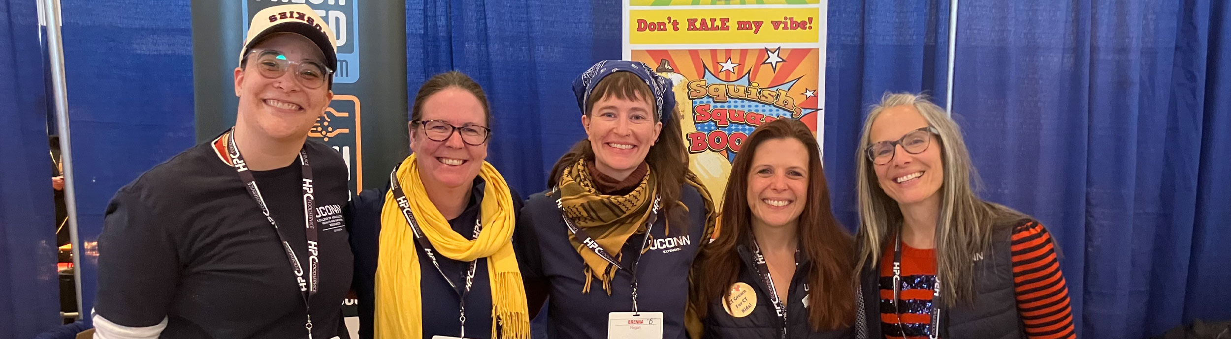 5 Farm to School regional coordinators standing behind a display table at an event.