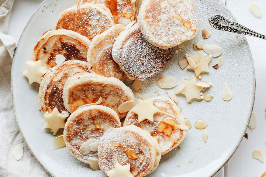 mini pancakes on a plate wiht syrup and powdered sugar.