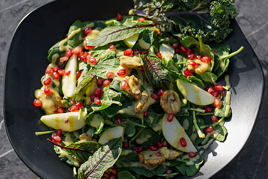 a green salad with apple slices and pomegranate seeds.