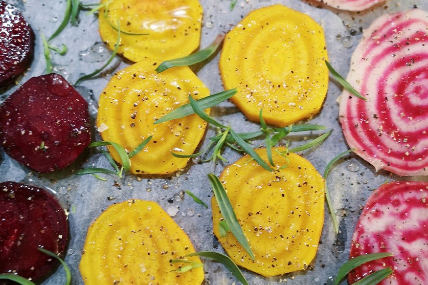 several varieties of beets sliced on a pan with rosemary to roast.
