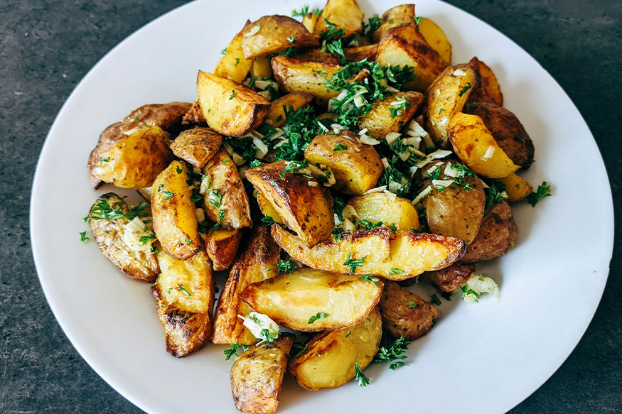 Roasted white potatoes with parsley and onion on a plate.