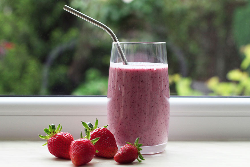 a smoothie in a glass with a straw and 4 strawberries next to it.